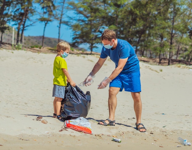 Volunteer blue face mask forest sand beach Son helps father hold black bag for pick up garbage Problem spilled rubbish trash planet pollution environmental protection Natural children education