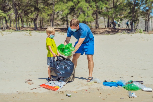 Volunteer blue face mask forest sand beach Son helps father hold black bag for pick up garbage Problem spilled rubbish trash planet pollution environmental protection Natural children education