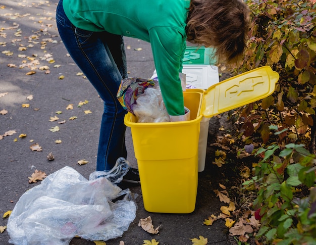 Volunteer girl sorts garbage in the street of the park. Concept of recycling.