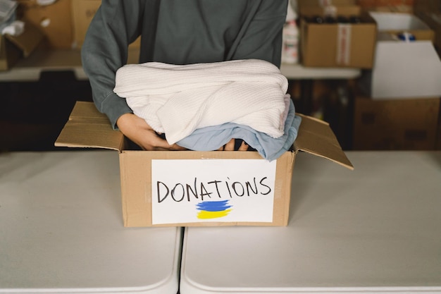 Volunteer teengirl preparing donation boxes for people in need in Ukraine Donation clothing for refugees from Ukraine support of war victims a box with the Ukrainian flagHumanitarian aid concept