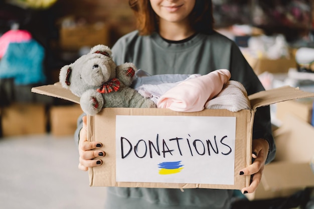 Volunteer teengirl preparing donation boxes for people in need in Ukraine Donation clothing for refugees from Ukraine support of war victims a box with the Ukrainian flagHumanitarian aid concept