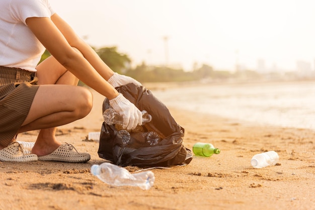 Volunteer woman picking plastic bottle into trash plastic bag black for cleaning the beach