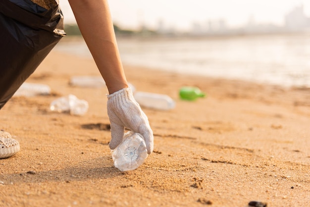 Volunteer woman picking plastic bottle into trash plastic bag black for cleaning the beach