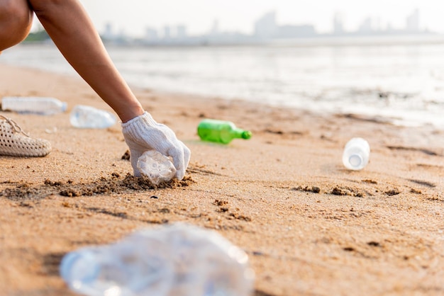 Volunteer woman picking plastic bottle into trash plastic bag black for cleaning the beach