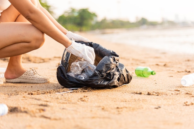 Volunteer woman picking plastic bottle into trash plastic bag black for cleaning the beach