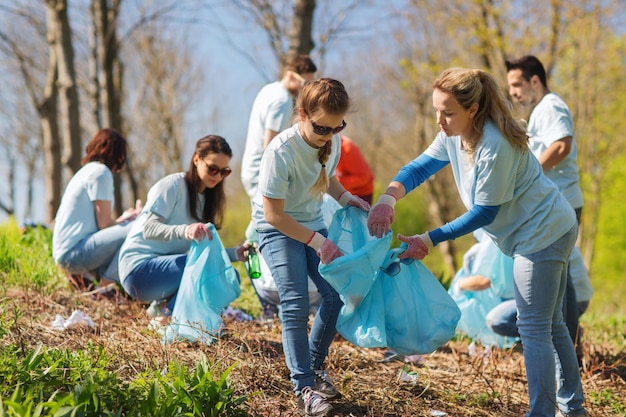 volunteering, charity, cleaning, people and ecology concept - group of happy volunteers with garbage bags cleaning area in park