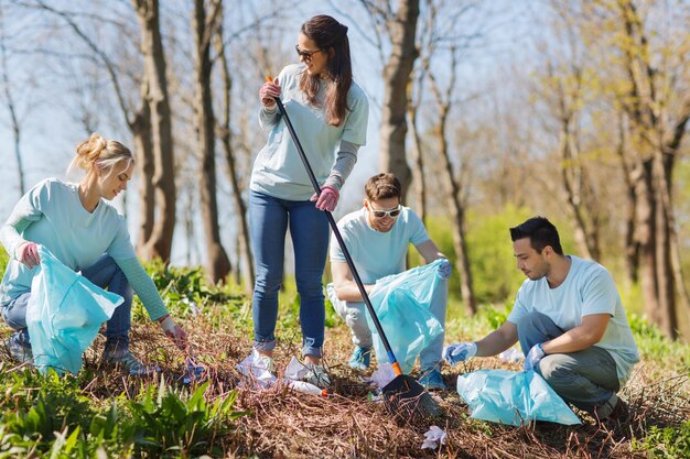 volunteering, charity, cleaning, people and ecology concept - group of happy volunteers with garbage bags cleaning area in park