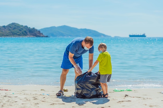 Volunteers blue face mask paradise beach sand lazur sea Father son pick up garbage into black bag Problem spilled rubbish trash planet pollution environmental protection Natural children education