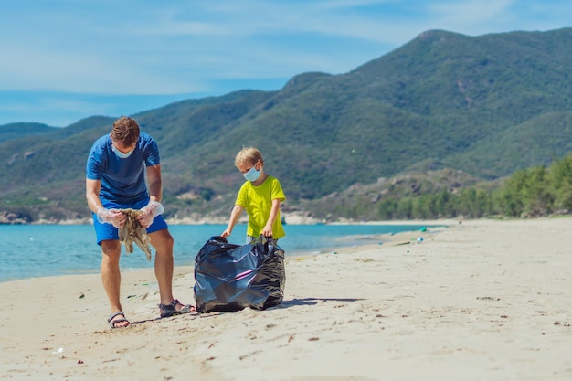 Volunteers blue face mask paradise beach sand lazur sea Father son pick up garbage into black bag Problem spilled rubbish trash planet pollution environmental protection Natural children education