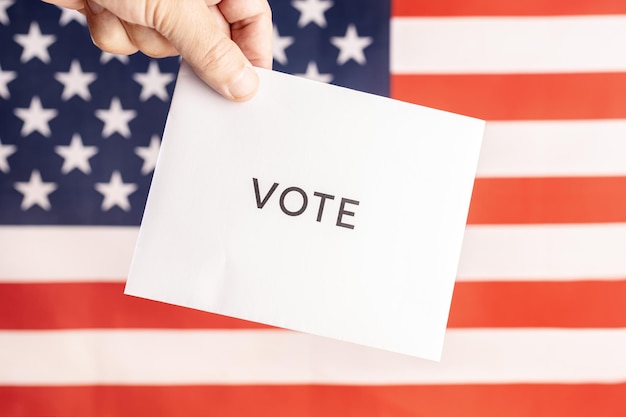 Vote Day concept Hand with ballot and United States flag at background