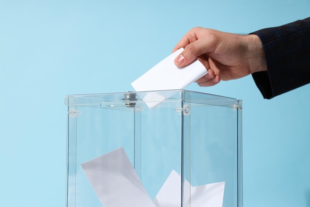 Voting box with papers and hand on blue background close up