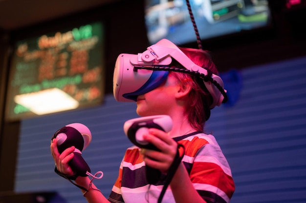 Vr game and virtual reality kid boy gamer six years old fun playing on futuristic simulation video game in 3d glasses and joysticks in entertainment vr room with innovation technology and neon light