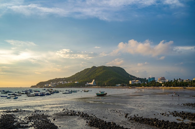 Vung Tau city aerial view with beautiful sunset and so many boats Panoramic coastal Vung Tau view from above with waves coastline streets coconut trees and Tao Phung mountain in Vietnam