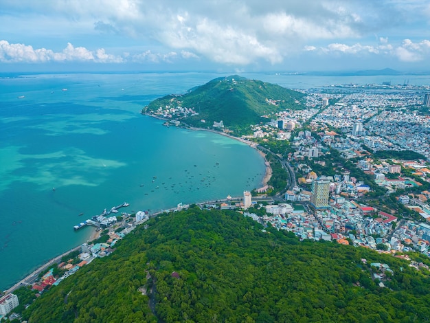 Vung Tau city aerial view with beautiful sunset and so many boats Panoramic coastal Vung Tau view from above with waves coastline streets coconut trees and Tao Phung mountain in Vietnam