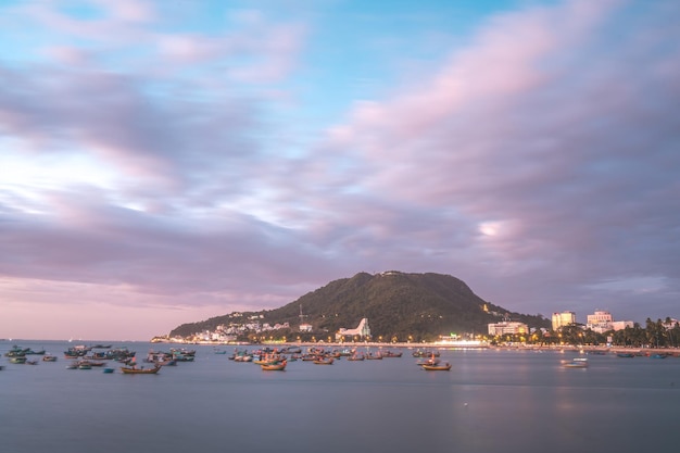 Vung Tau city aerial view with beautiful sunset and so many boats Panoramic coastal Vung Tau view from above with waves coastline streets coconut trees and Tao Phung mountain in Vietnam