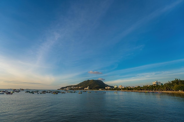 Vung Tau city aerial view with beautiful sunset and so many boats Panoramic coastal Vung Tau view from above with waves coastline streets coconut trees and Tao Phung mountain in Vietnam