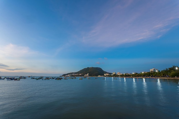 Vung Tau city aerial view with beautiful sunset and so many boats Panoramic coastal Vung Tau view from above with waves coastline streets coconut trees and Tao Phung mountain in Vietnam