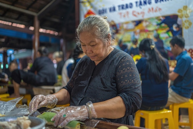 Vung Tau VIETNAM JAN 12 2023 Focus old woman with traditional Vietnamese dress ao ba ba Making wrapping Tet Cake the Vietnamese lunar new year Tet food outdoor by hands