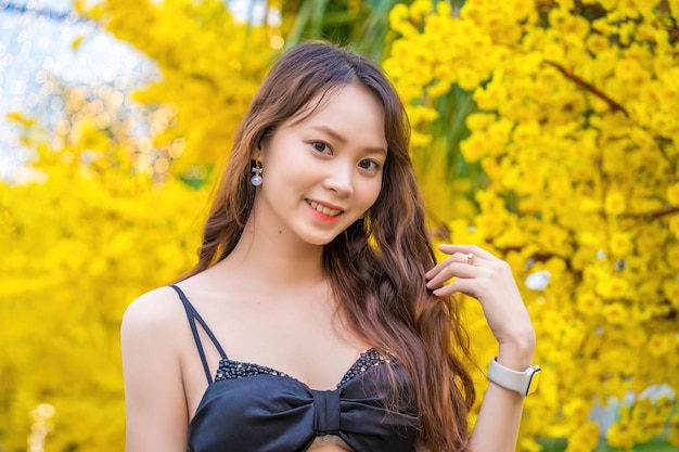 Vung Tau VIETNAM JAN 7 2023 Portrait of a beautiful Asian woman on black dress standing near Ochna Integerrima flower Tet holiday Lunar New Year