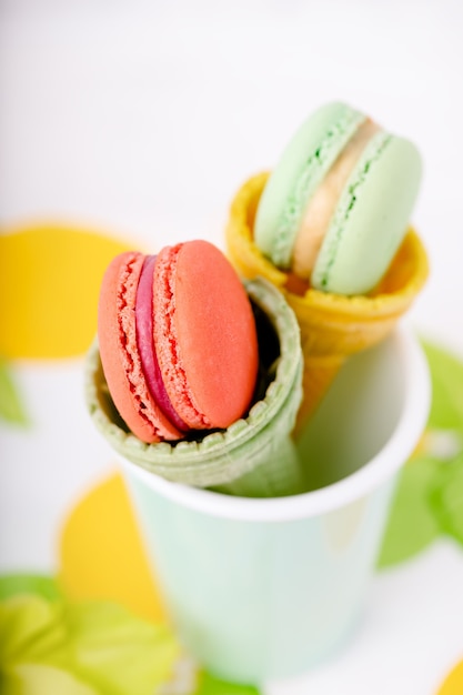 Wafer cup for ice cream with macarons and green gladiolus on a light marble background, copy space