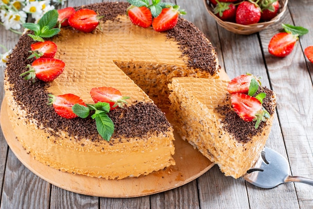 Waffle cake with condensed milk cocoa and butter garnished with strawberries on a wooden table