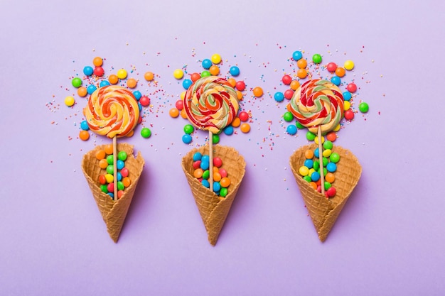 Waffle cone full of assorted traditional candies falling out on colored background with copy space Happy Holidays sale concept