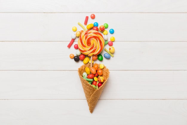 waffle cone full of assorted traditional candies falling out on colored background with copy space Happy Holidays sale concept