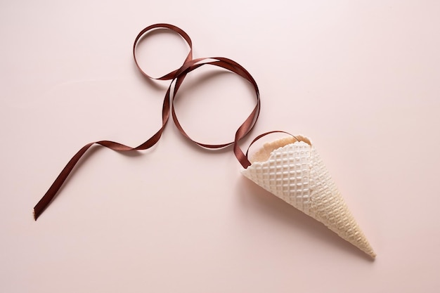 Waffle cone with brown ribbon in the shape of 8 on a beige background. Concept for March 8. 8 years old, birthday, holiday