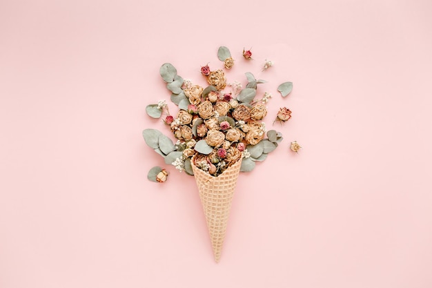 Waffle cone with cotton bouquet and eucalyptus leaves on pink background flat lay top view