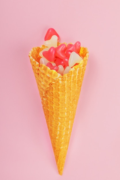 Waffle cone with gummy hearts on a pink background. vertical frame