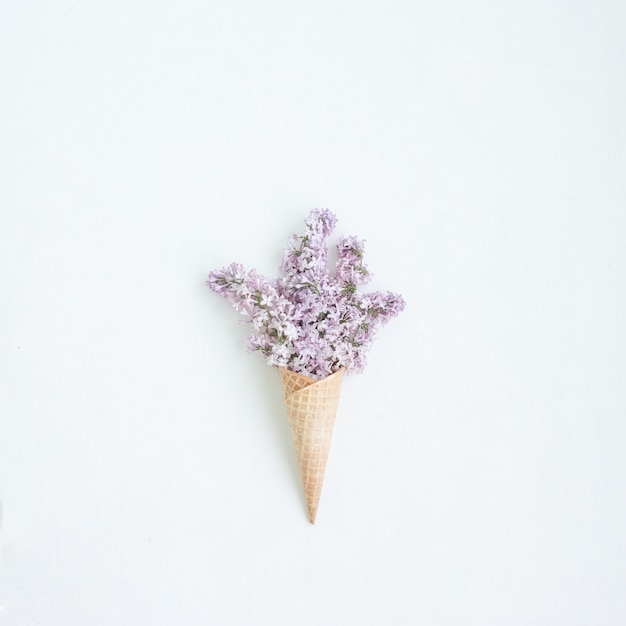 Waffle cone with lilac on white background, flat lay, top view