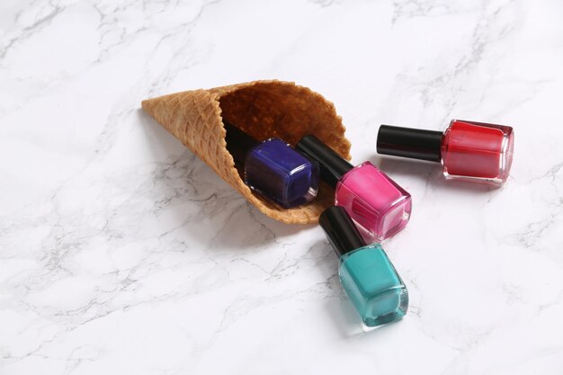 Waffle cones with nail polish bottles on a marble background Creative beauty layout