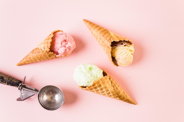 Waffle ice cream cones with plate of ice cream scoops on a pink background.