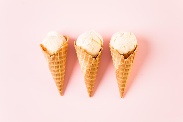 Waffle ice cream cones with plate of ice cream scoops on a pink background.