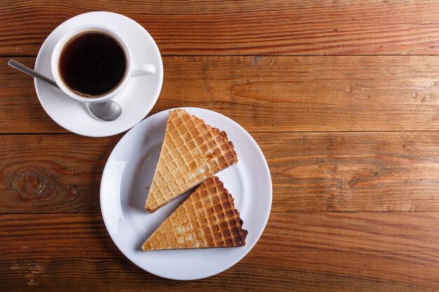 Waffle sandwiches with boiled condensed milk in plate on brown wooden table with cup of coffee. top view