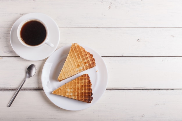 Waffle sandwiches with boiled condensed milk in plate on white wooden table with cup of coffee. top view