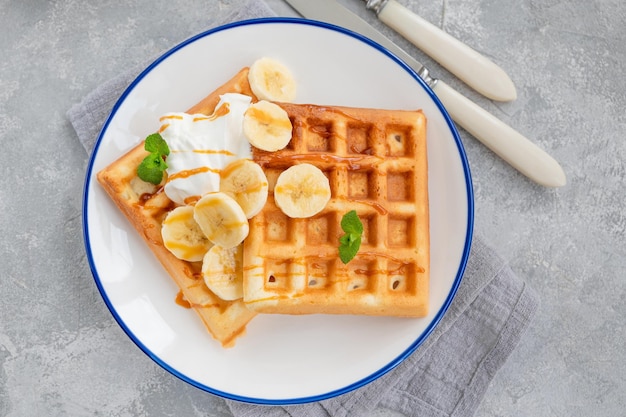 Waffles with banana whipped cream and salty caramel on a gray concrete background