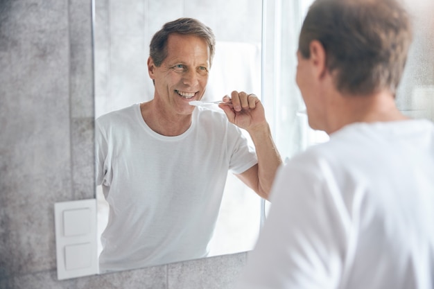 Waist up man with a toothbrush smiling at himself in the mirror