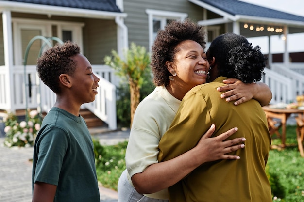 Waist up portrait of african american family embracing while welcoming guests for summer party outdo