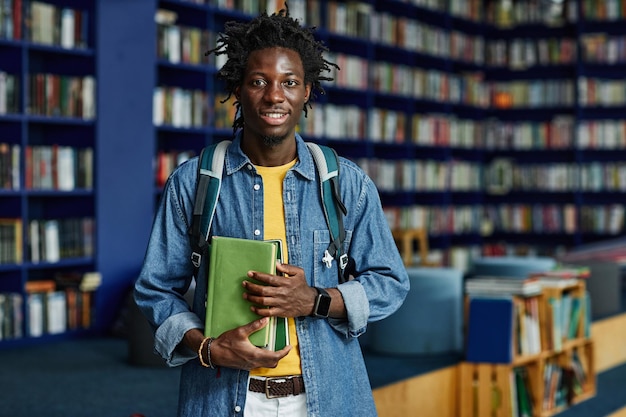 Waist up portrait of black young man with backpack standing in library and looking at camera copy sp