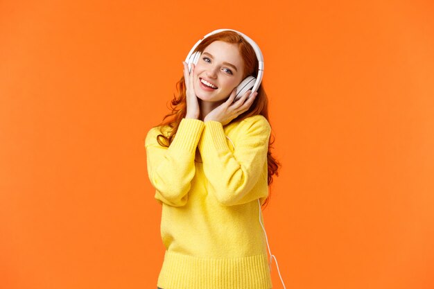 Waist-up portrait cute teenage redhead woman in white headphones, tilt head listen music