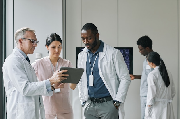 Waist up portrait of diverse group of doctors looking at digital tablet during council or conference