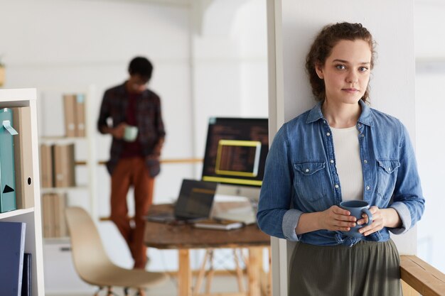 Photo waist up portrait of female it programmer looking at camera while coding mug with computer code in background, copy space