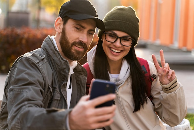 Waist up portrait of glad young loving couple enjoying date at the street while cuddling and making selfie with happiness at the modern smartphone