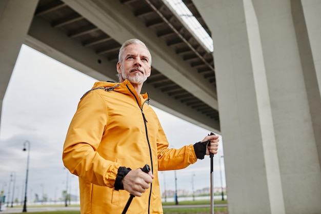 Waist up portrait of handsome mature man enjoying nordic walk with poles in urban city setting copy