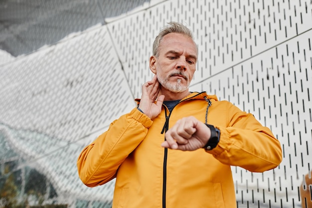 Waist up portrait of handsome mature man exercising outdoors and tracking pulse rate with fitness wa