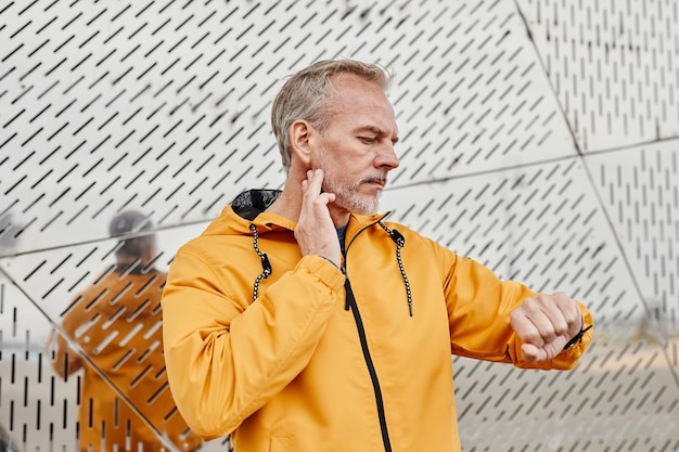 Waist up portrait of handsome mature man tracking pulse rate with fitness watch while exercising out