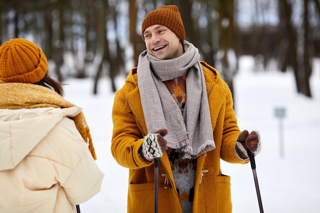 Waist up portrait of happy couple skiing in winter forest focus on carefree young man with ski poles