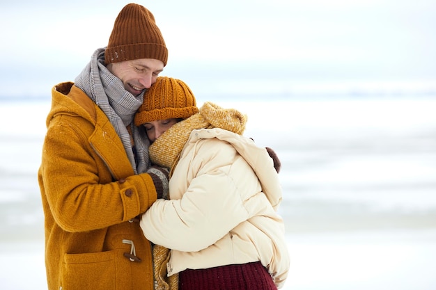 Waist up portrait of loving young couple embracing in minimal winter landscape copy space