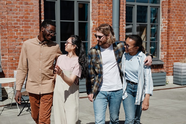 Waist up portrait of modern young people walking in city street lit by sunlight, all wearing sunglasses